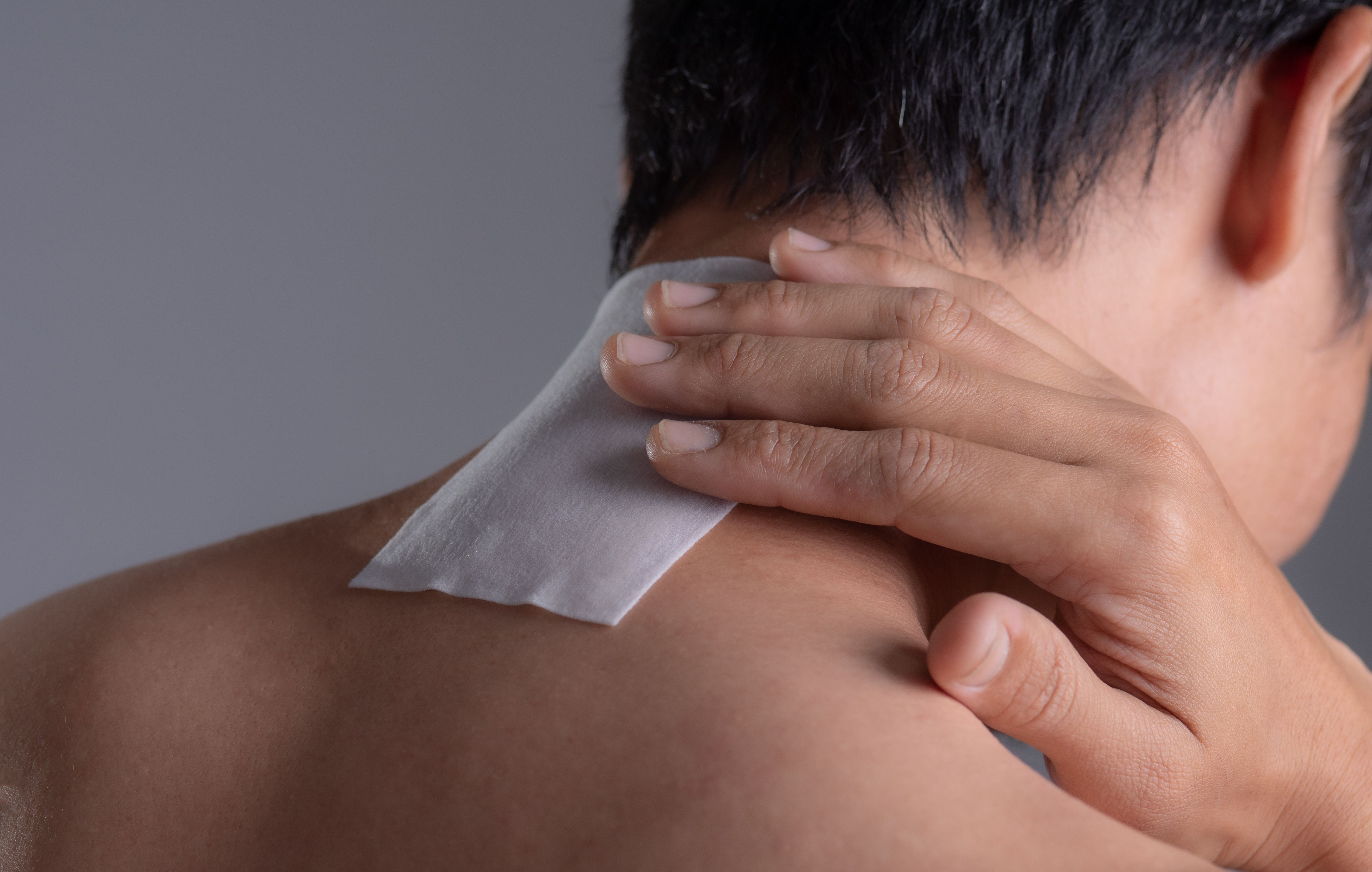 Man holding his hand over a pain relief patch on the back of his neck