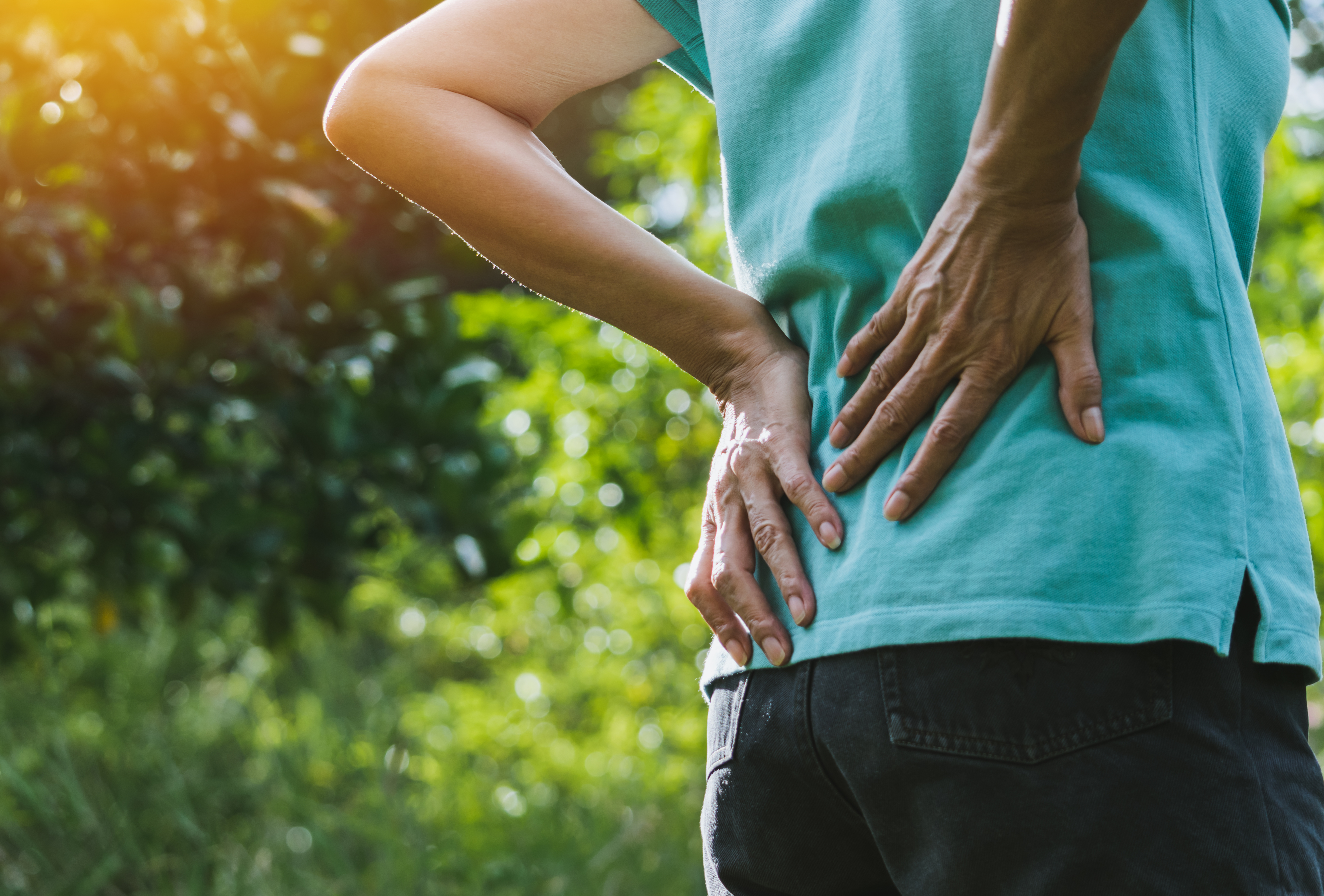 Person holding their back in pain while in the woods