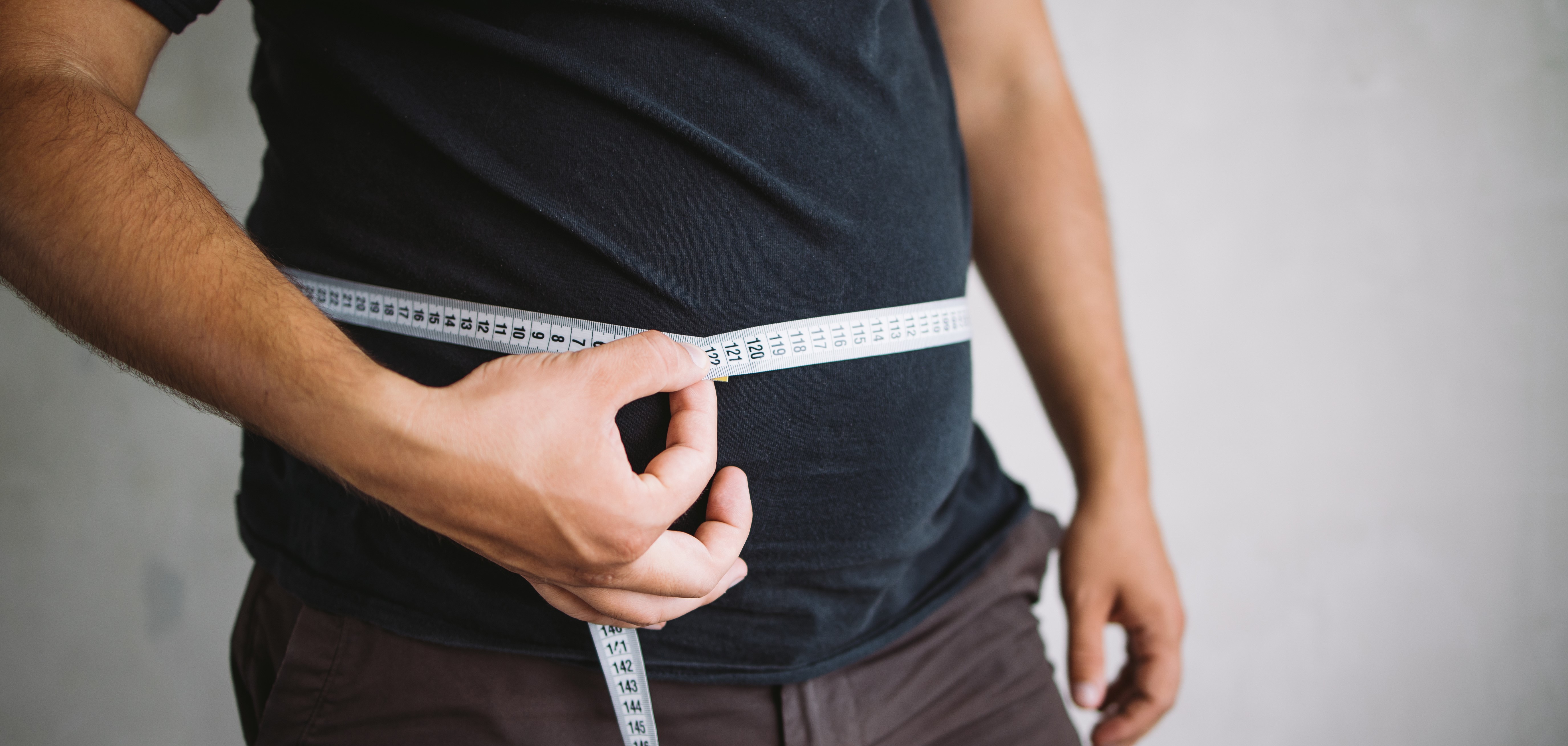 Overweight man measuring waist with measure tape, close up image