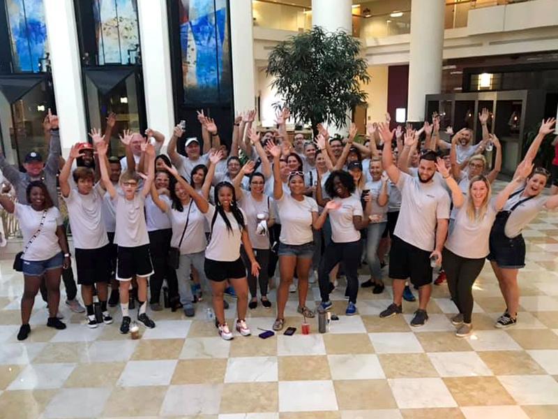 Group of people smiling with their hands raised standing within a hotel lobby