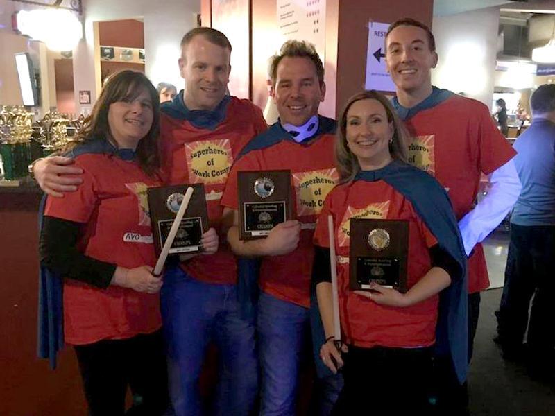 Group of people smiling while wearing superhero capes holding plaques