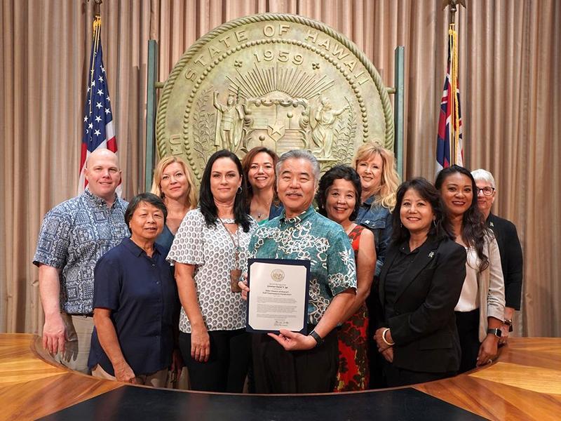 Group of people holding a plaque in front of the State of Hawaii seal