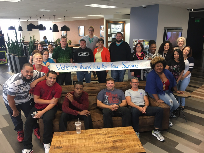 Group of people smiling while sitting and standing in a office common area