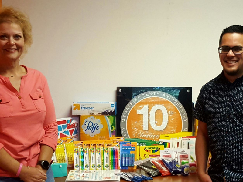 Man and woman smiling beside table filled with school supplies