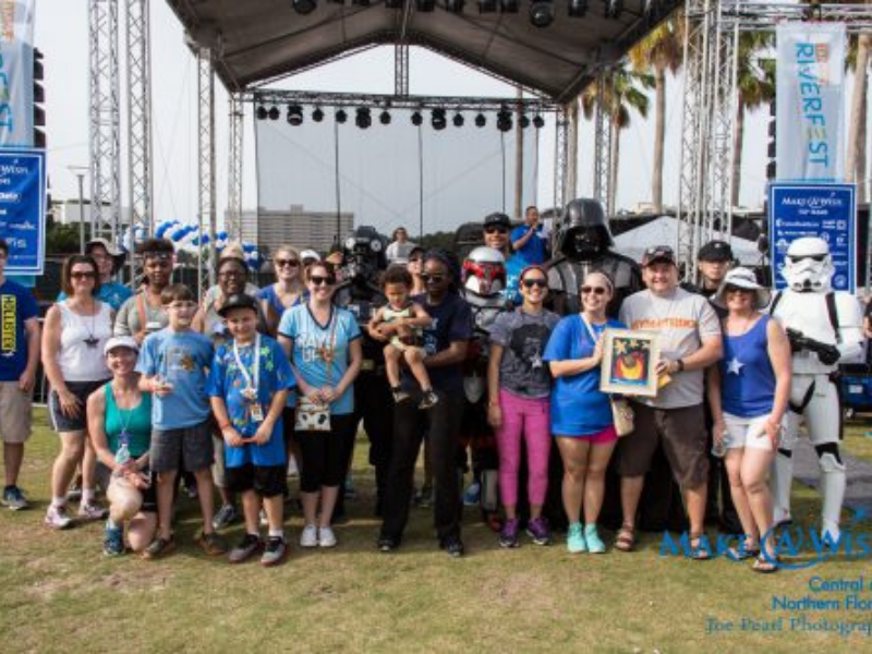 Group of adults and children smiling beside a Star Wars Storm Trooper at an outside venue