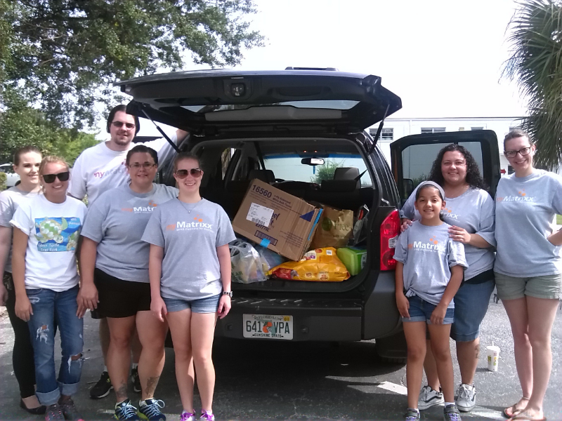 Group of MyMatrixx employees standing beside open car trunk filled with supplies