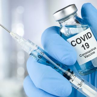Healthcare cure concept with a hand in blue medical gloves holding Coronavirus, Covid 19 virus, vaccine vial