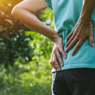 Person holding their back in pain while in the woods