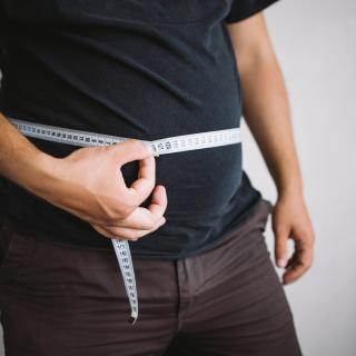 Overweight man measuring waist with measure tape, close up image
